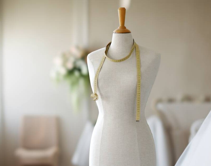 A mannequin with a measuring tape wrapped around the neck in a studio. Elegant fabric can be seen to the right.