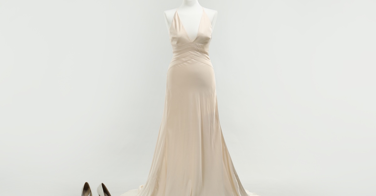 A mannequin showcases an off-white wedding dress that reaches the floor. A pair of white shoes sits beside it.