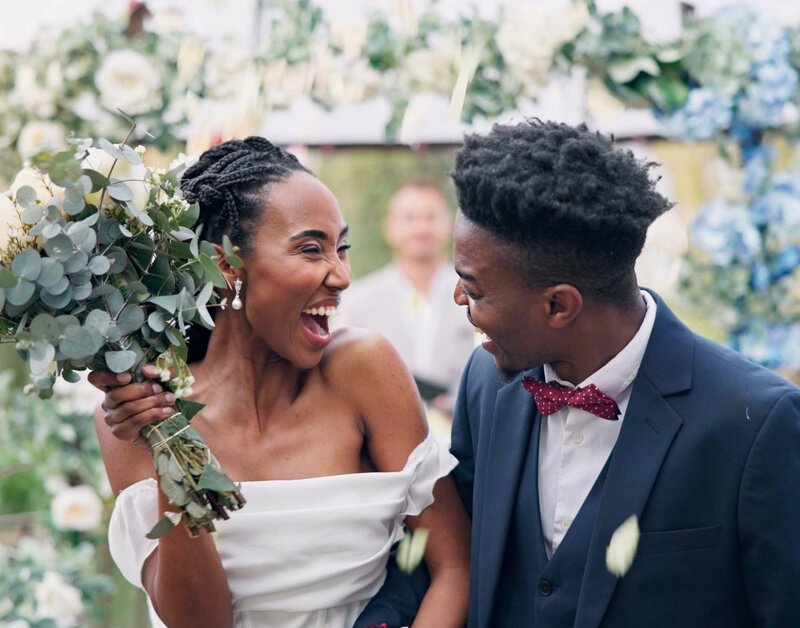 A young black couple smiles with happiness as they return from the altar of their beautiful garden ceremony.