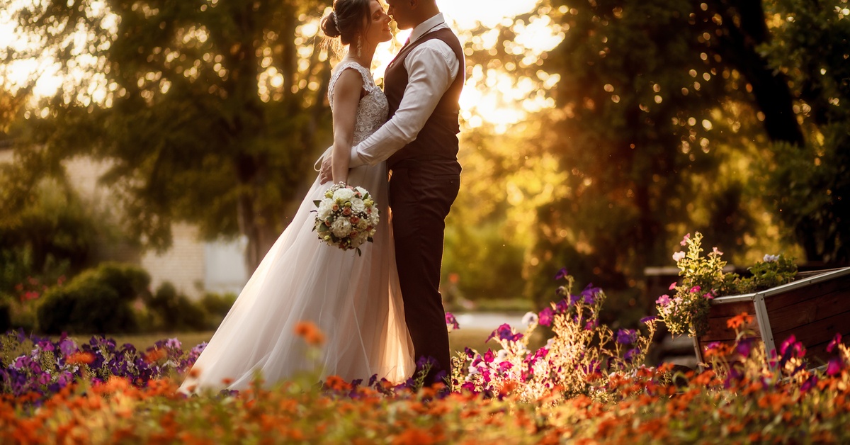 A groom holds his bride closely by the waist during golden hour in a garden as they stare into each other.