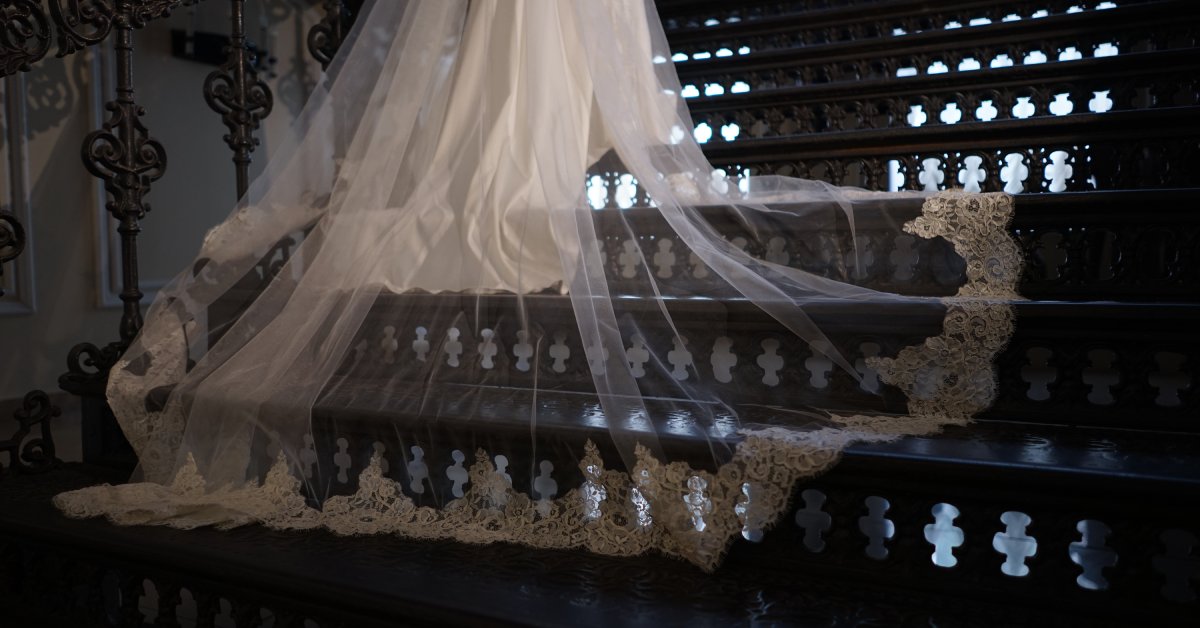 A low-angle view of a wedding gown's train lying on iron stairs. The top layer forms a thin, transparent veil.